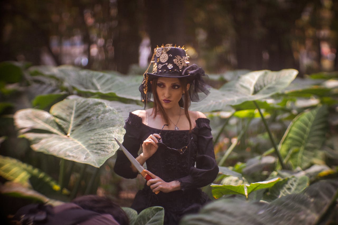 A woman in a mystical costume stands in a lush forest holding a dagger.